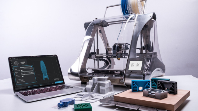 A 3D printer with a spool of filament and a laptop displaying rocket design software, highlighting the playful side of civil engineering.