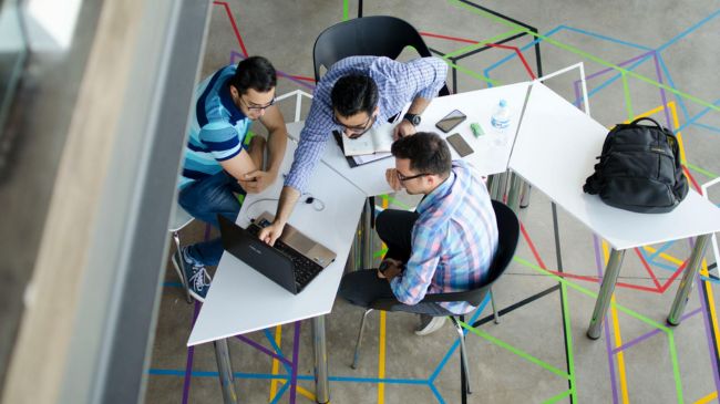 Three professionals collaborating at a round table with a laptop, discussing a BIM project for efficient project management in civil engineering.