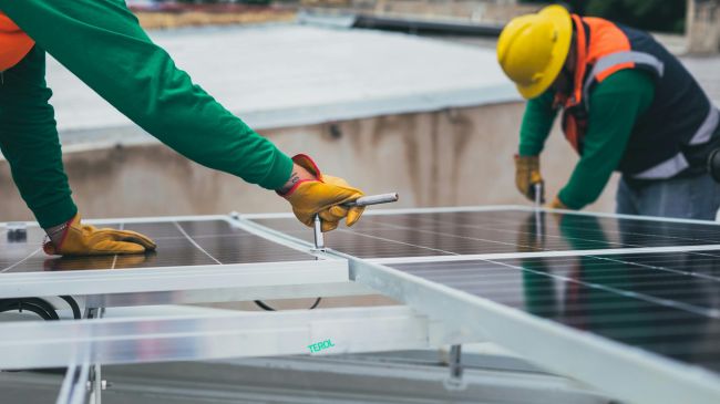 Two workers in safety gear installing solar panels on a rooftop, highlighting renewable energy infrastructure.