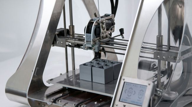 A 3D printer in the midst of creating a grey, interlocking structure, showcasing the precision of additive manufacturing