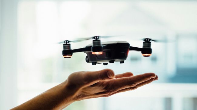 Advanced compact drone with red navigation lights hovering above a human hand, symbolizing modern technologies in engineering.