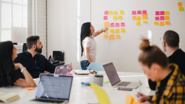 A diverse team engaged in a strategy session on water reuse and management, with a woman pointing at various ideas on sticky notes.