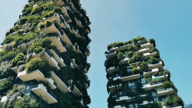 Two residential towers in Milan, known as Bosco Verticale, covered with lush greenery and various plants on their balconies.